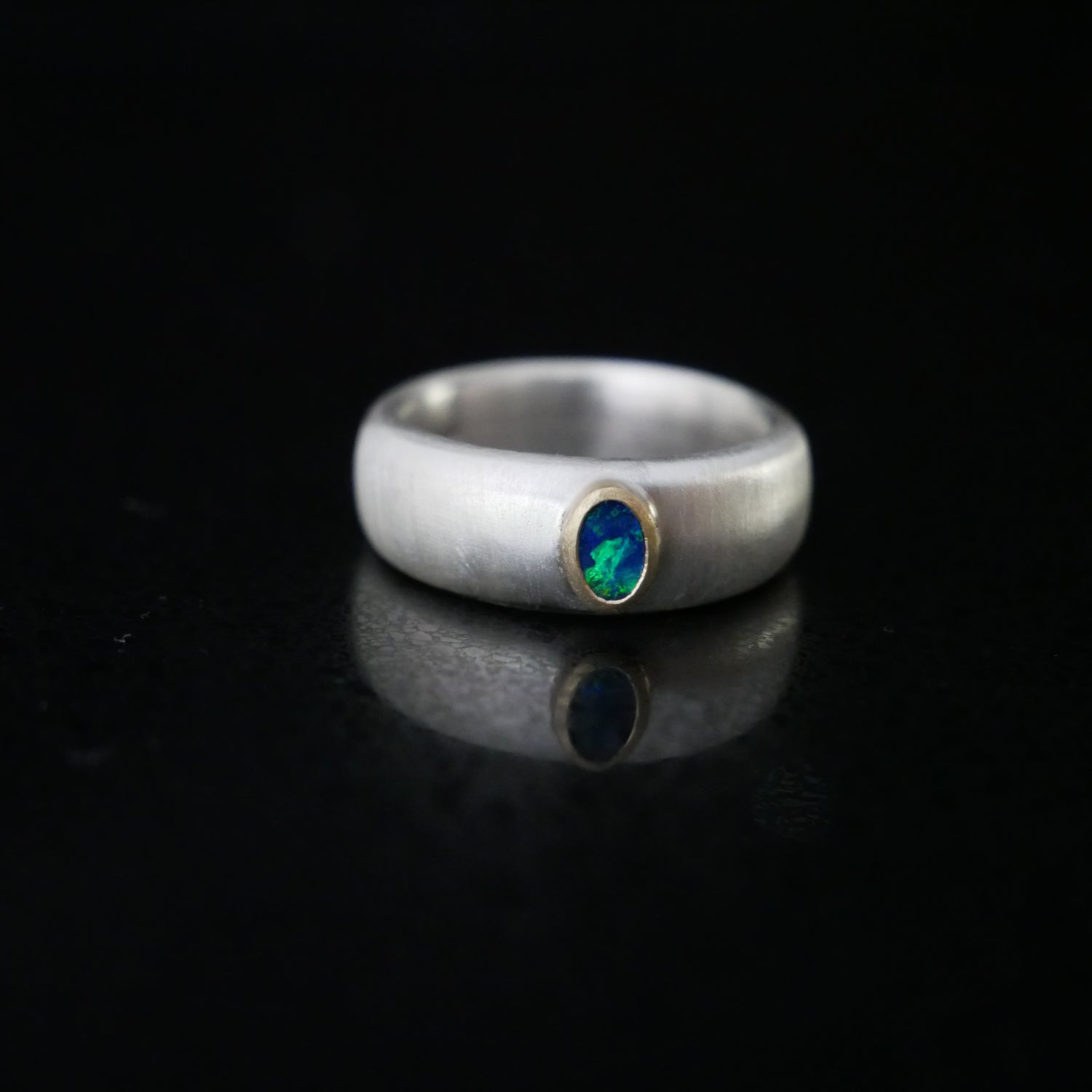 tiny oval opal set in 18ct gold on a wide silver ring